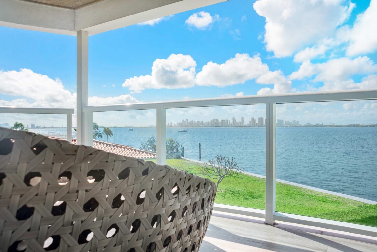 Covered waterfront balcony with cushioned outdoor seating, glass railings, expansive bay views, and a covered design that provides a comfortable outdoor space for enjoying the water, skyline scenery, and surrounding tropical landscape.