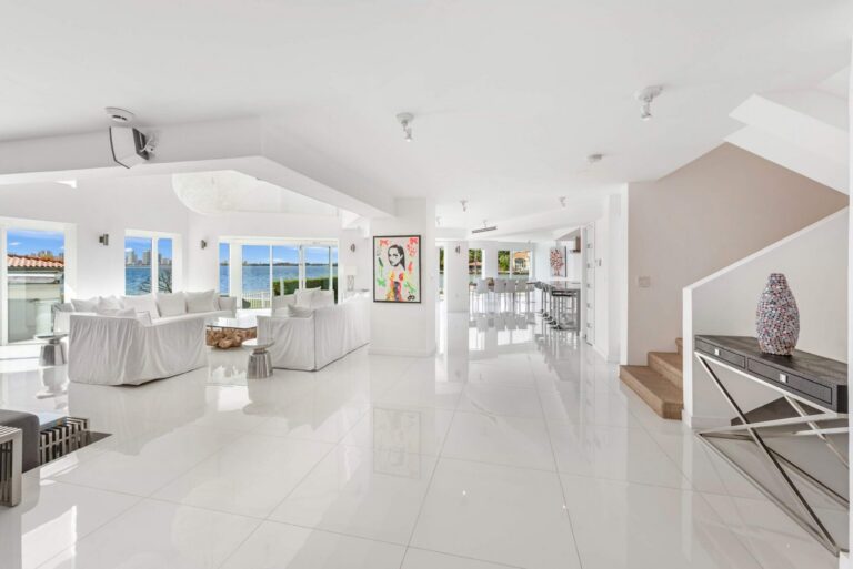 Expansive open-concept main level featuring glossy tile flooring, multiple waterfront seating areas, contemporary artwork, abundant natural light, and seamless flow between the media lounge, kitchen, dining area, and gathering spaces.