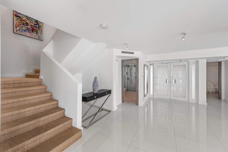 Spacious entry level featuring a carpeted staircase, private elevator, built-in storage closets, glossy tile flooring, and contemporary furnishings. Functional transition space providing easy access to guest rooms and shared living areas.