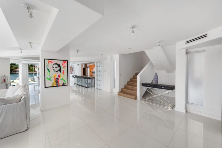 Open foyer featuring glossy tile flooring, contemporary artwork, staircase access, breakfast bar seating, and an open-concept layout. Bright transitional space connects the kitchen, living room, dining area, and guest accommodations.