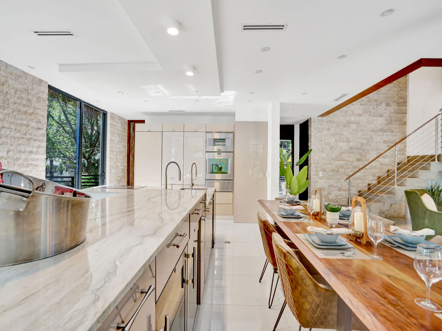 Spacious chef’s kitchen featuring an oversized island with bar seating, sleek cabinetry, and extensive counter space. Large windows provide natural light and tropical views, while the open layout connects seamlessly to the dining and living areas.
