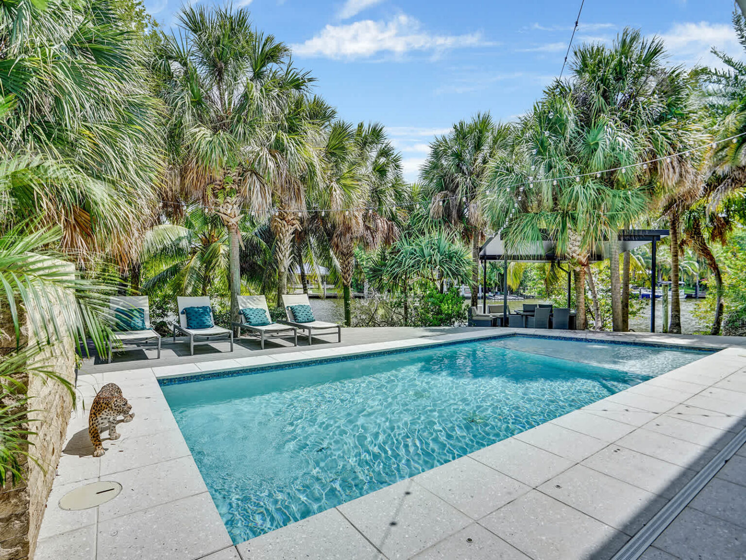 Private swimming pool surrounded by tropical landscaping and mature palm trees. Features a spacious tiled sun deck, lounge chairs, and tranquil garden views, creating a peaceful outdoor space for relaxation and recreation.