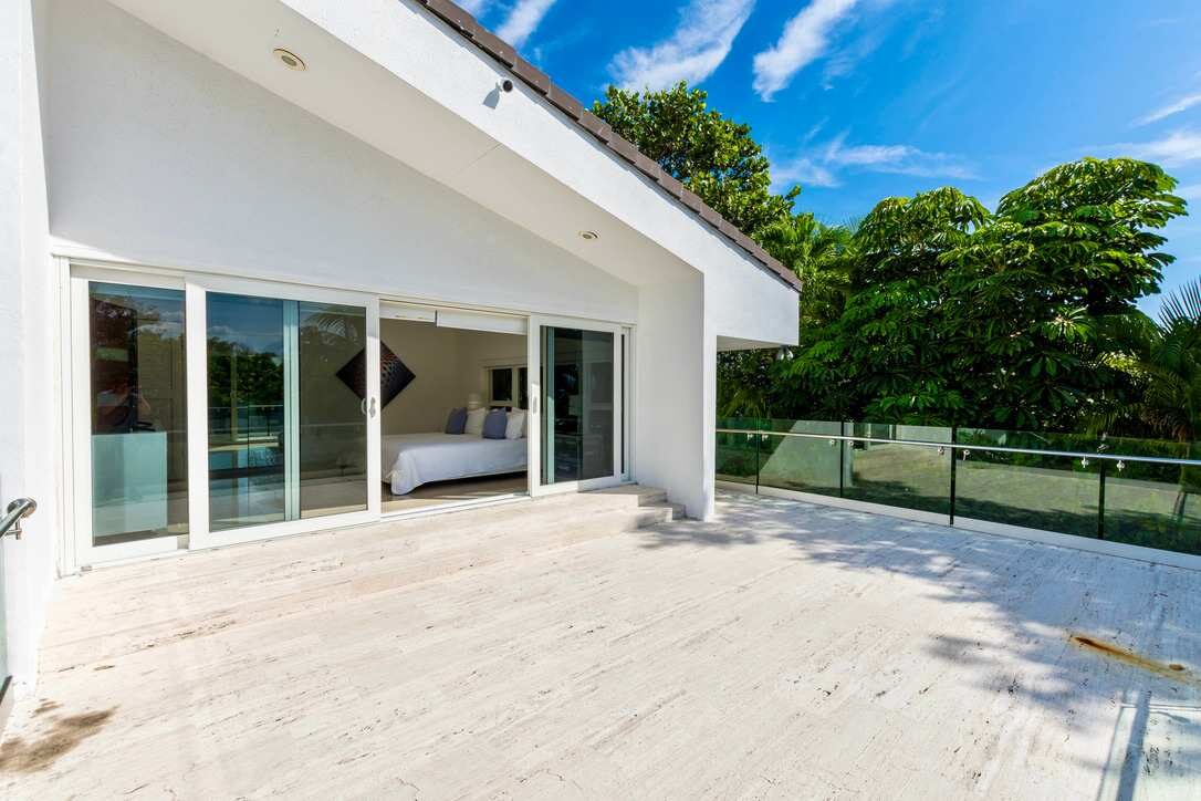 Private rooftop terrace featuring an expansive outdoor deck, glass balcony railing, direct access from the primary bedroom, tropical garden views, and ample space for outdoor seating, relaxation, and enjoying the surrounding landscape.