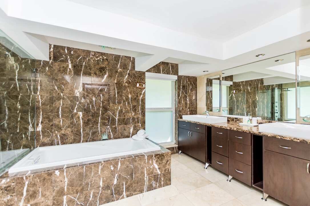 Luxury primary bathroom featuring a soaking tub, double-sink vanity with extensive counter space, floor-to-ceiling marble finishes, oversized wall mirrors, built-in cabinetry, recessed lighting, and a spacious spa-inspired layout with premium fixture