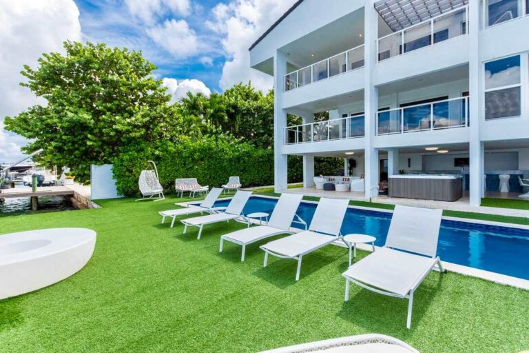 Waterfront villa outdoor area with a private swimming pool, sun loungers, artificial turf lawn, landscaped tropical greenery, covered patio space, multiple balconies, and direct access to poolside relaxation and entertainment areas.