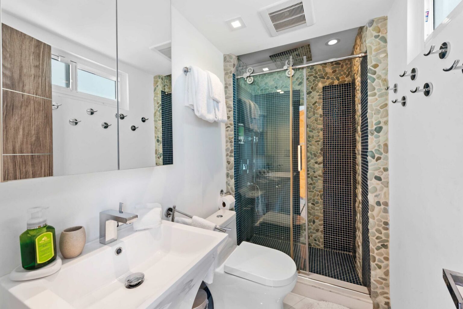 Contemporary guest bathroom featuring a single-sink vanity, glass-enclosed walk-in shower, decorative mosaic tile accents, modern fixtures, wall-mounted towel storage, and a functional layout designed for comfort and daily convenience.