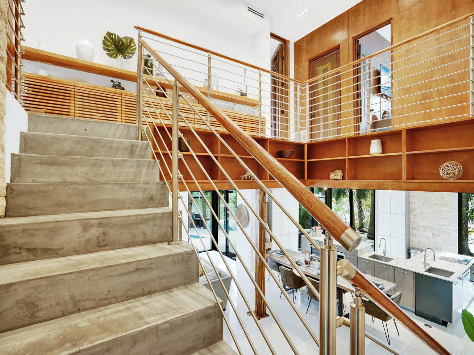Architectural staircase featuring natural stone steps, wood accents, and modern metal railings. The open multi-level design overlooks the main living area, while large windows and contemporary finishes create a bright, airy interior.