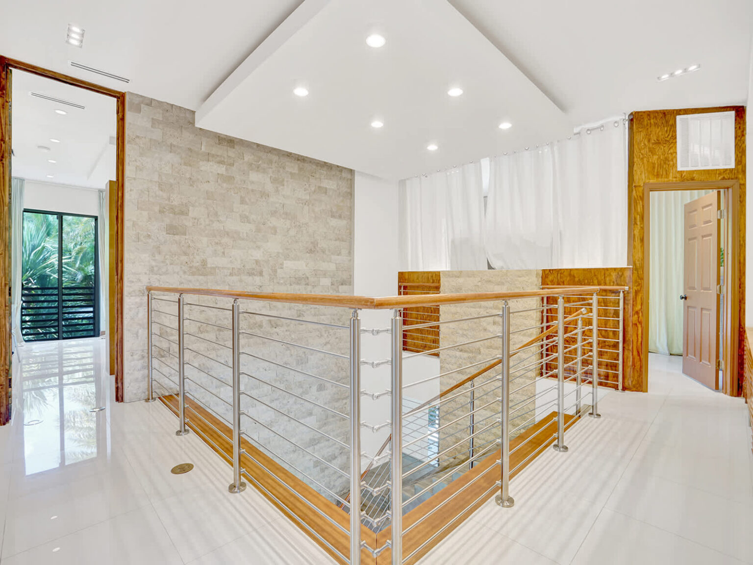Second-floor landing with modern metal railings, recessed lighting, and natural stone accent walls. The open design overlooks the main living area, while clean architectural lines and bright finishes create an airy, contemporary feel.