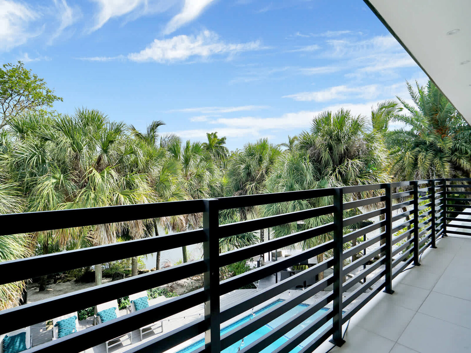 Second-floor balcony with modern metal railings and elevated views of tropical palm trees and the pool area below. This outdoor space offers a peaceful setting to enjoy natural surroundings, fresh air, and garden scenery.