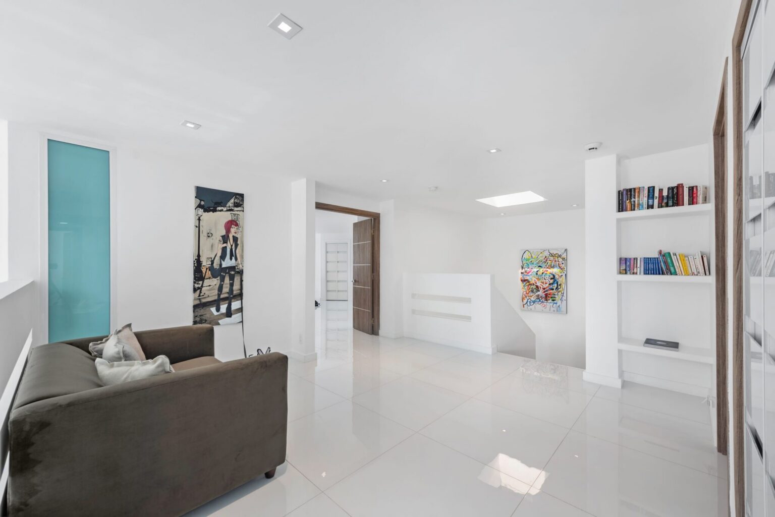 Bright upper-level lounge featuring built-in bookshelves, contemporary artwork, sofa seating, recessed lighting, tile flooring, and an open-concept layout connecting bedrooms and common areas, with flexible space for reading, relaxing, or gathering.