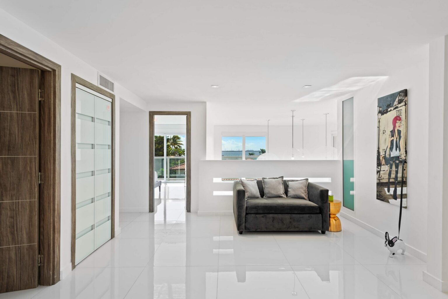 Upper-level sitting area featuring a contemporary sofa, tile flooring, recessed lighting, modern artwork, and an open-concept layout. Bright common space connects bedrooms and balconies while providing room for relaxation and conversation.