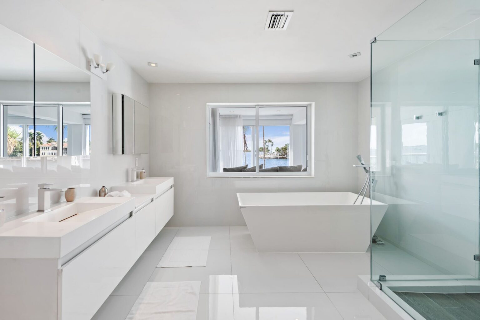 Spa-style primary bathroom featuring a freestanding soaking tub, double-sink vanity, glass-enclosed walk-in shower, oversized mirror, tile flooring, and a bright open layout with natural light and dedicated grooming space.