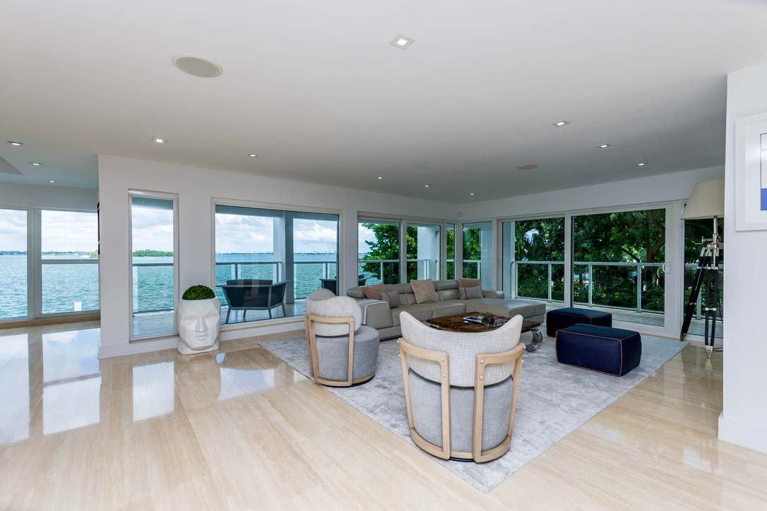 Corner living area featuring panoramic water-view windows, multiple lounge chairs, a large sectional sofa, area rug, recessed lighting, tile flooring, and an open-concept layout with abundant natural light and waterfront vistas.