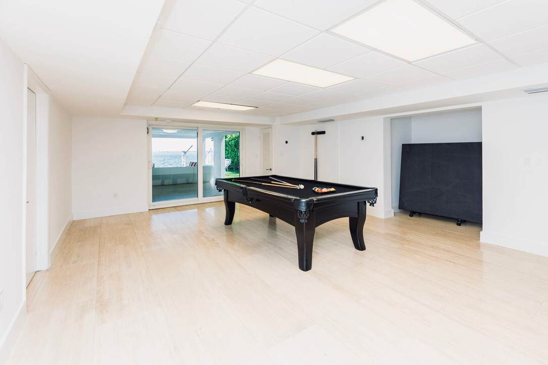 Recreation room featuring a full-size pool table, wood-look flooring, suspended ceiling lighting, sliding glass doors, and a spacious open layout designed for games, entertainment, and indoor gathering space with direct outdoor access.