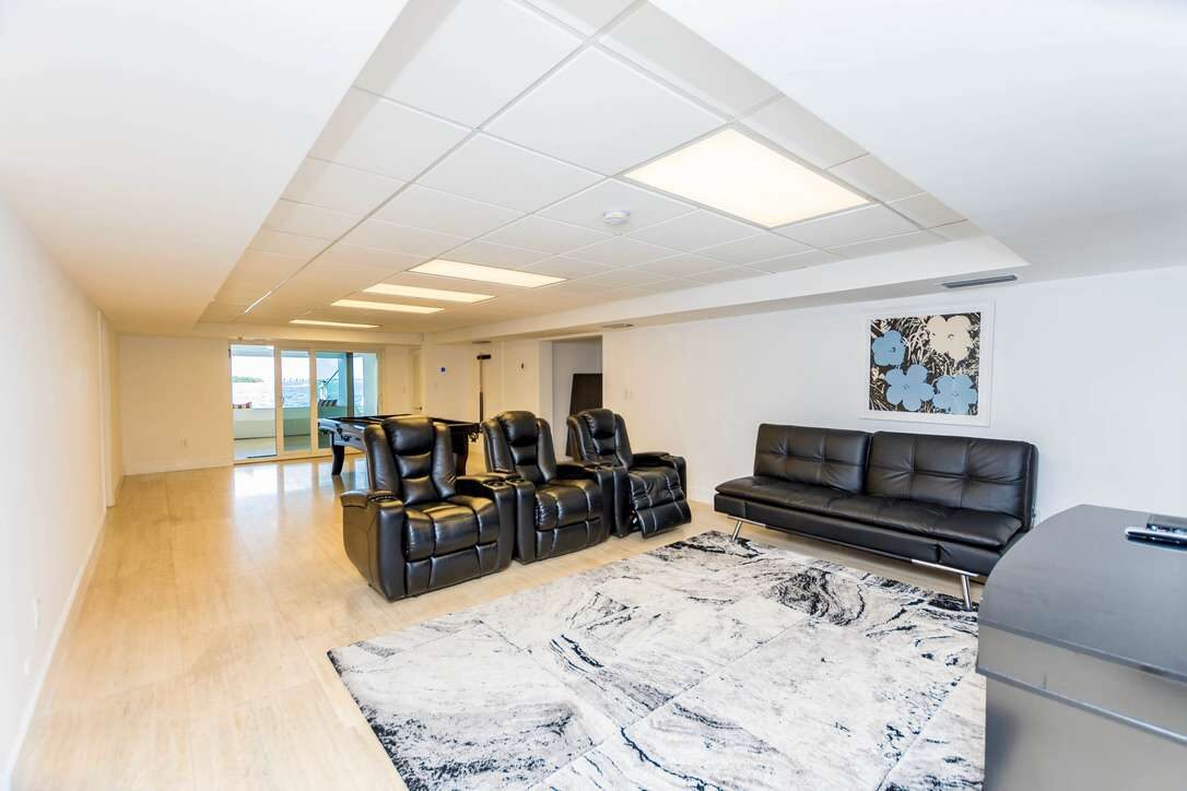 Private home theater area featuring multiple recliner chairs, a large flat-screen TV, leather sofa seating, area rug, wood-look flooring, suspended ceiling lighting, and a spacious entertainment layout designed for movie nights and group gatherings.