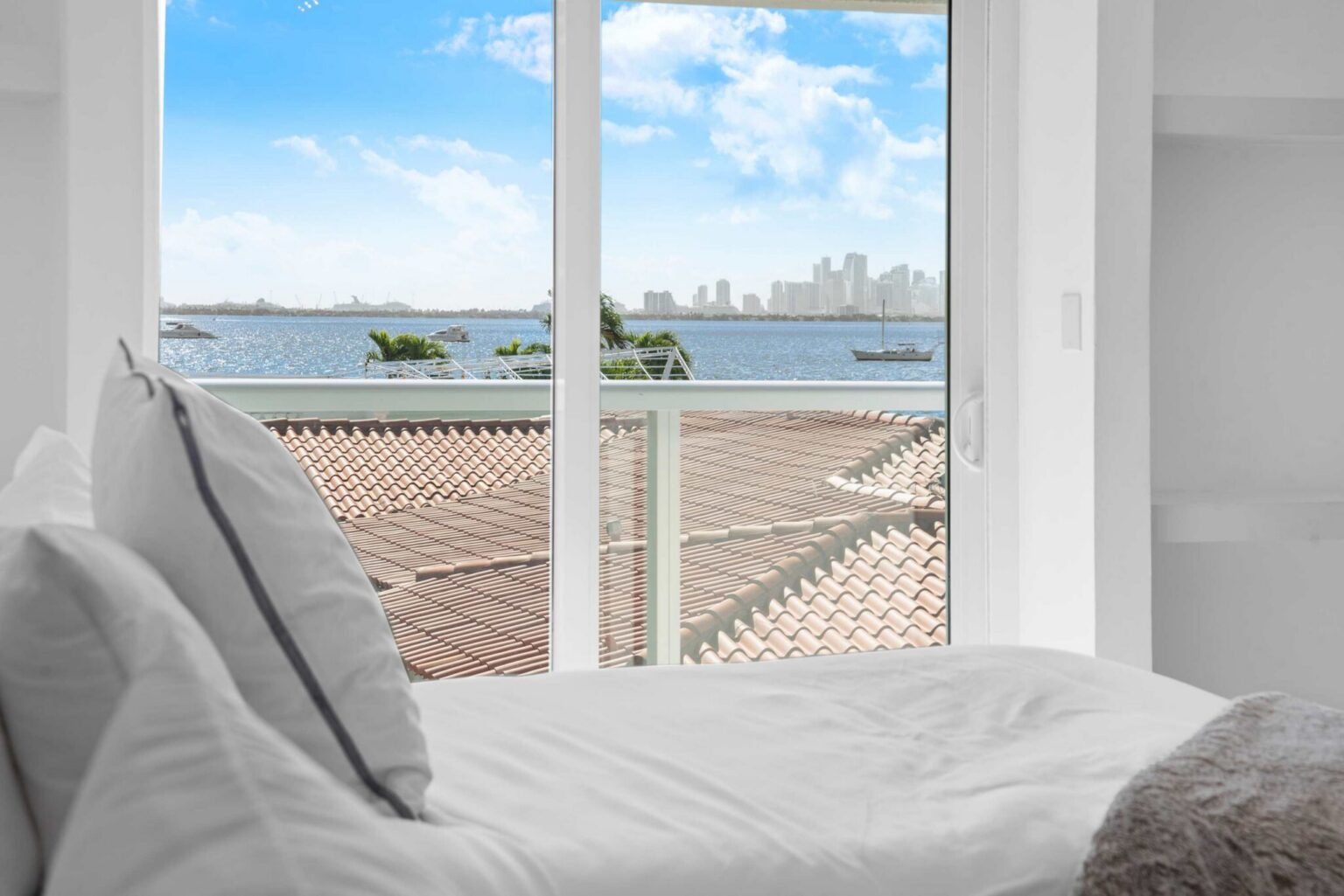 Water-view bedroom outlook featuring expansive bay views through large picture windows, abundant natural light, and a serene vantage point overlooking the waterfront and distant city skyline from the comfort of the bedroom suite.