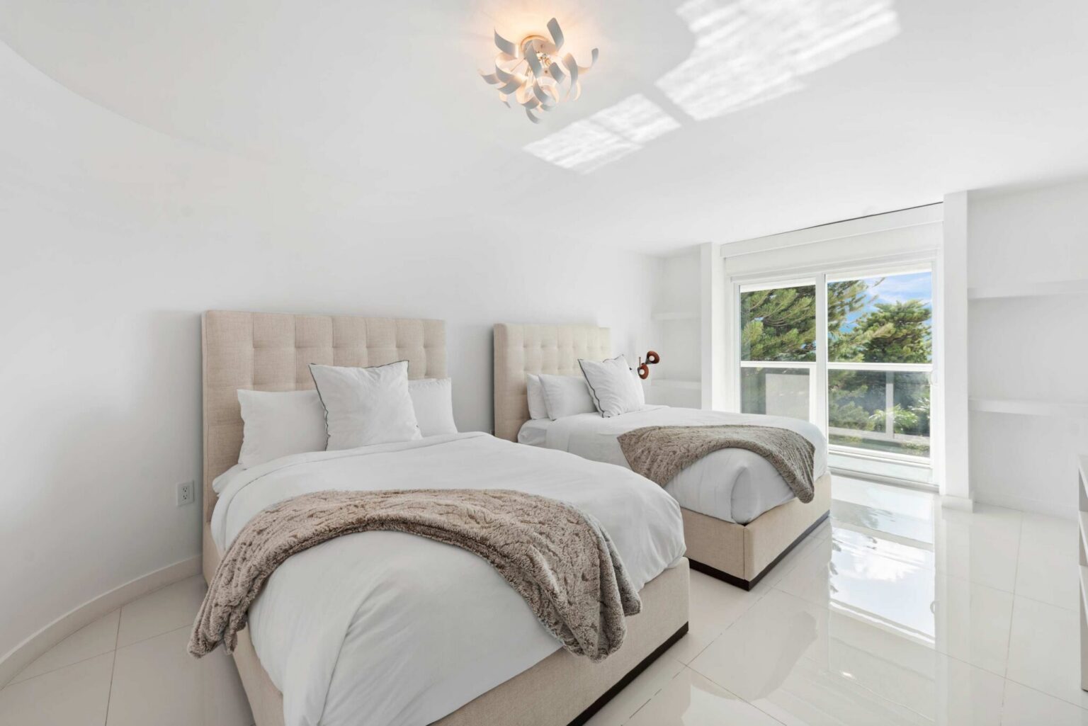 Twin guest bedroom featuring two upholstered twin beds with premium linens, a large window with natural light, tile flooring, recessed lighting, and a bright contemporary layout designed for flexible sleeping arrangements and guest comfort.