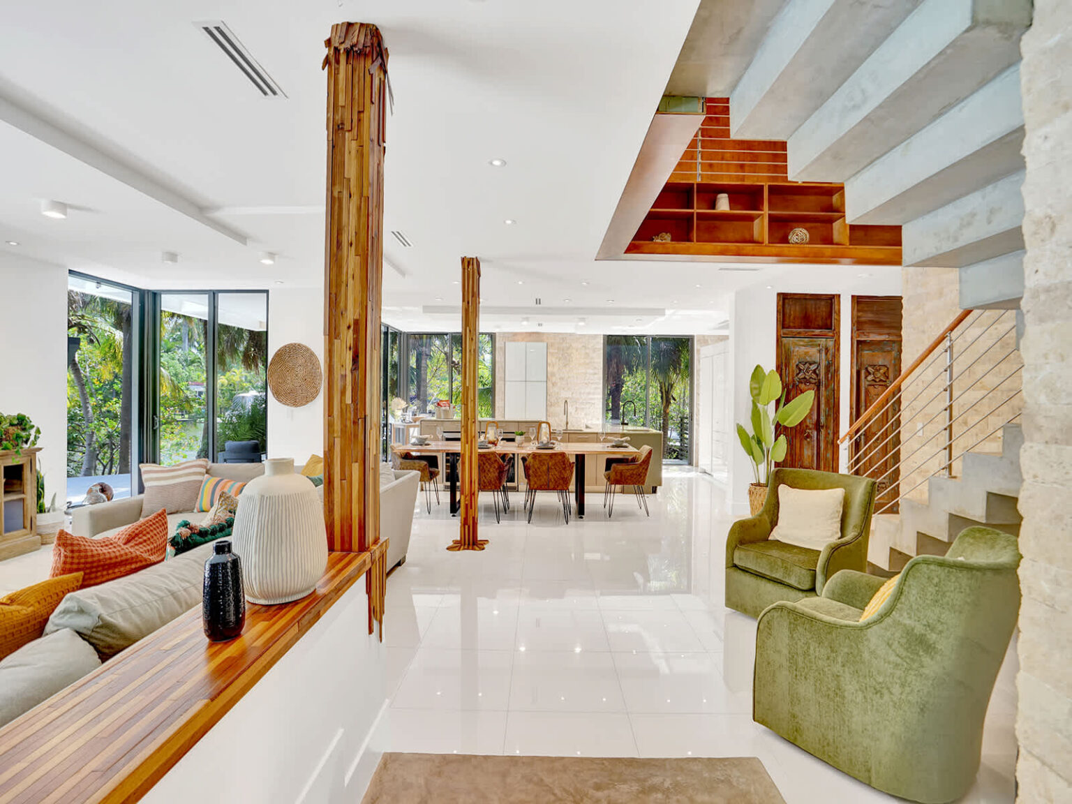Spacious open-concept living area with high ceilings, polished tile floors, and natural wood architectural details. Floor-to-ceiling windows provide abundant natural light, while the layout connects seamlessly to the dining area and outdoor spaces.