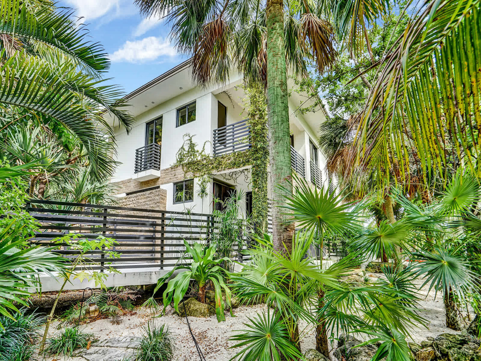 Exterior view of the contemporary two-story villa surrounded by mature palm trees and lush tropical landscaping. Modern architecture, elevated living spaces, and abundant greenery create a private setting with a seamless connection to nature.