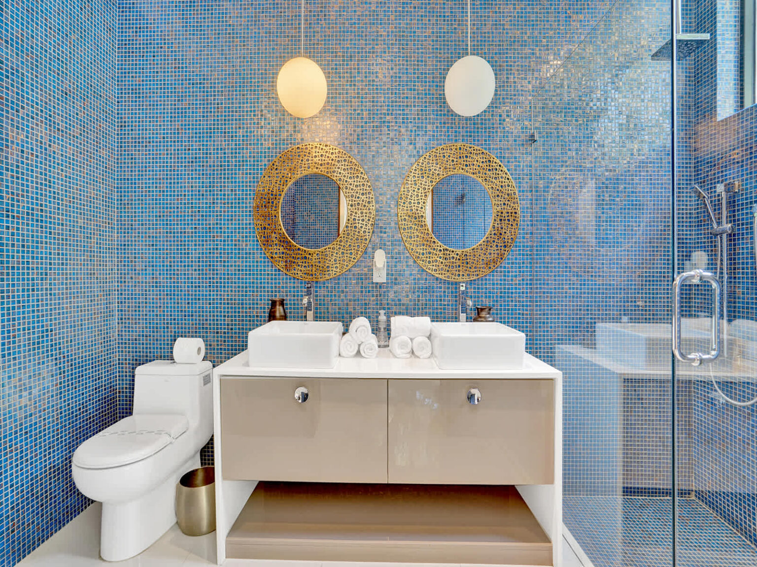 Contemporary ensuite bathroom featuring a double vanity, dual vessel sinks, and decorative blue tile walls. Large framed mirrors, modern lighting, and generous counter space create a bright, functional, and well-appointed layout.