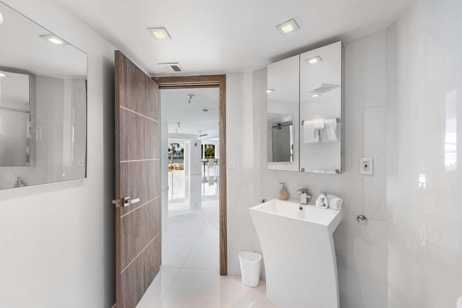 Modern powder room featuring a contemporary pedestal sink, wall-mounted mirror, sleek tile finishes, recessed lighting, and convenient access to the main living areas. Bright, minimalist design with clean architectural details.