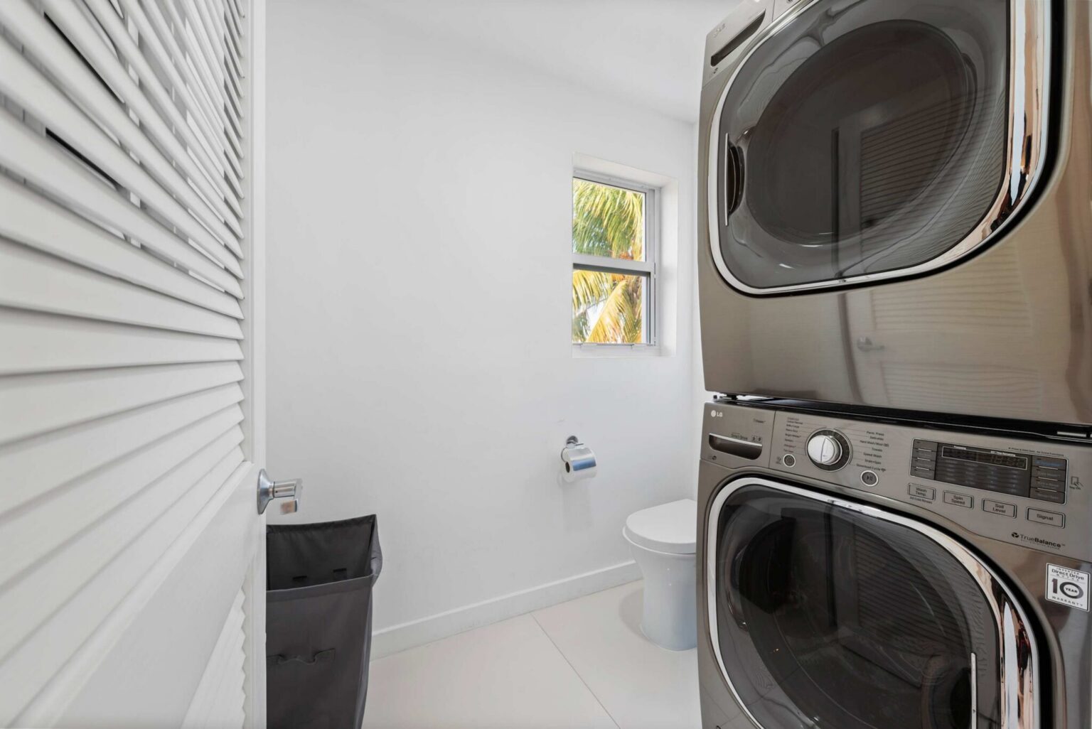 Laundry room featuring a full-size stacked washer and dryer, utility sink, window for natural light, tile flooring, storage space, and a dedicated area for laundry, cleaning supplies, and extended-stay convenience.