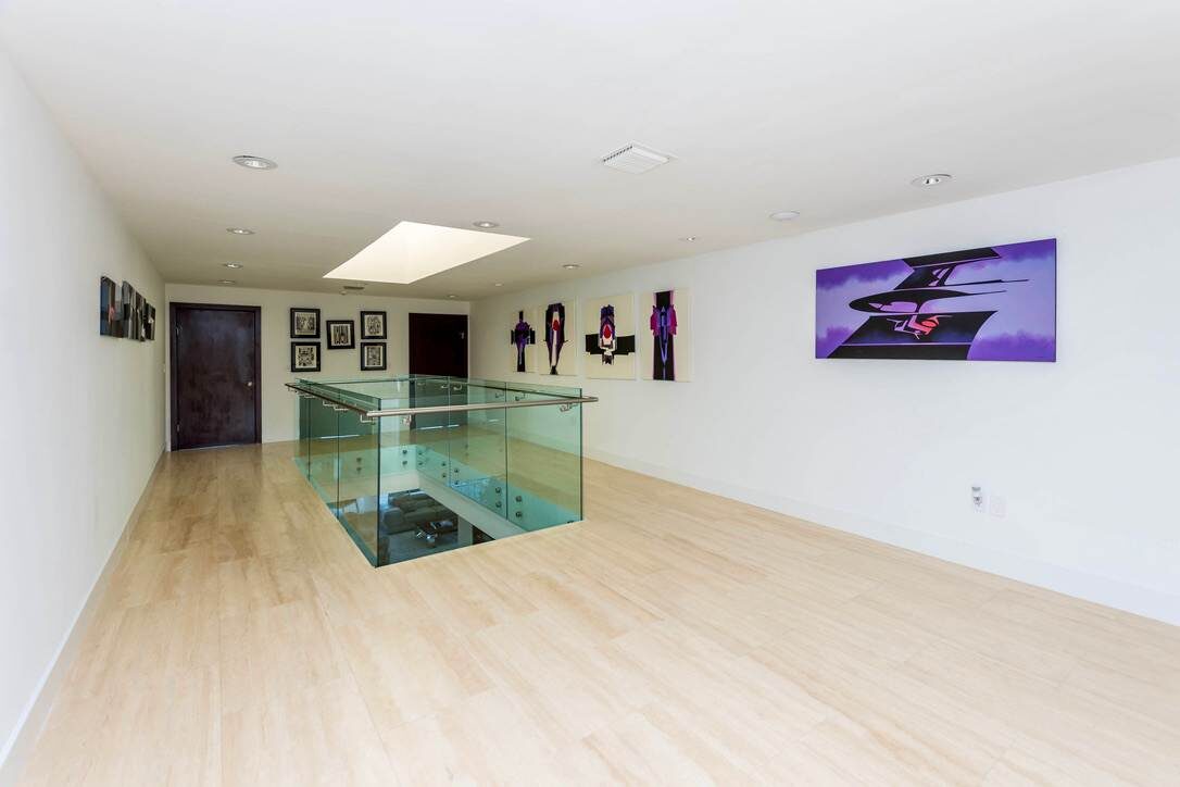 Upper-level gallery space featuring glass stairwell railings, oversized tile flooring, recessed lighting, contemporary artwork, a skylight feature, and an open hallway layout connecting bedrooms, living areas, and multiple levels of the home.