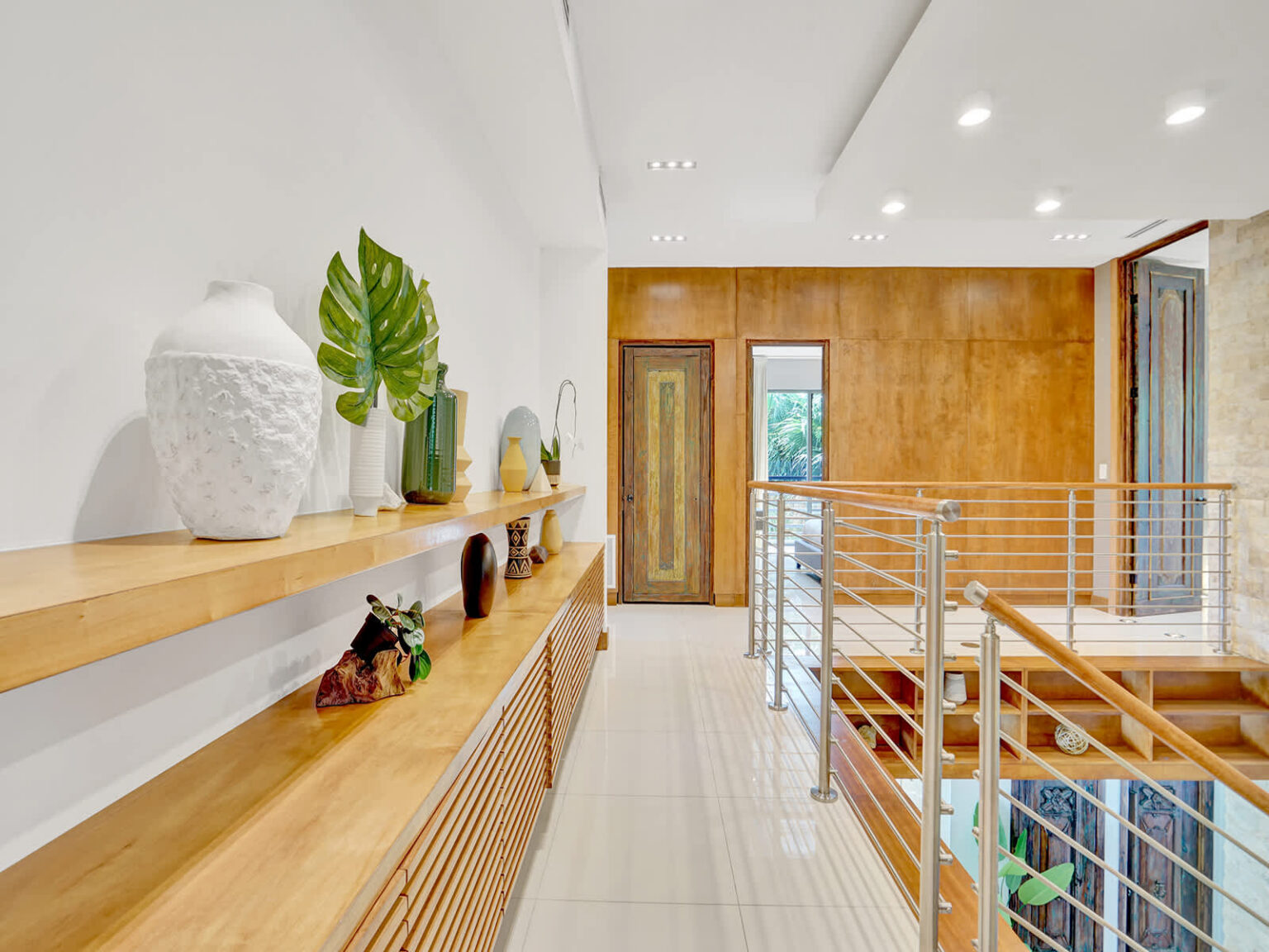 Second-floor hallway featuring custom wood cabinetry, modern metal railings, and recessed lighting. The open layout overlooks the living area below, while natural materials and clean architectural details enhance the contemporary design.