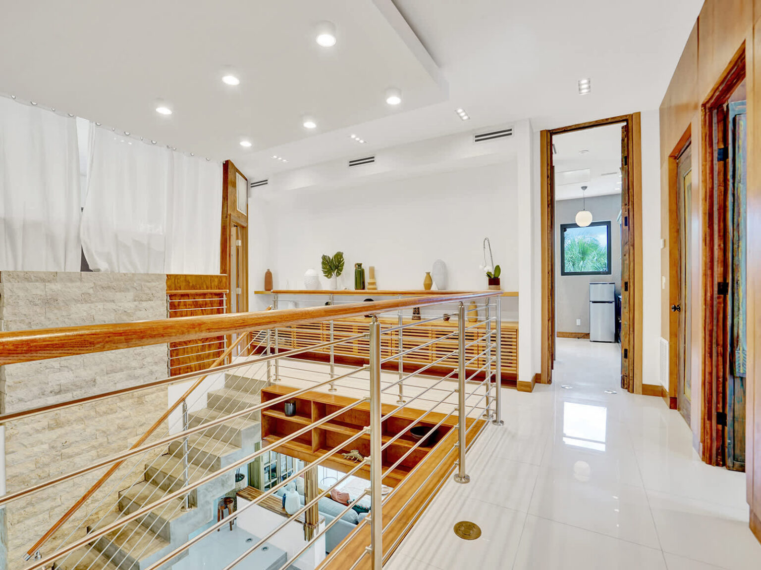 Open second-floor landing with modern metal railings, recessed lighting, and views overlooking the main living area. Natural stone accents, clean architectural lines, and bright finishes create a spacious, contemporary interior.