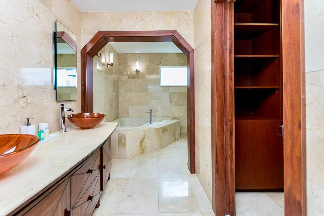 Primary bathroom suite featuring a double vanity with vessel sinks, natural stone finishes, built-in storage cabinetry, oversized soaking tub, large wall mirrors, and direct access to a spacious walk-in closet with custom organization systems.
