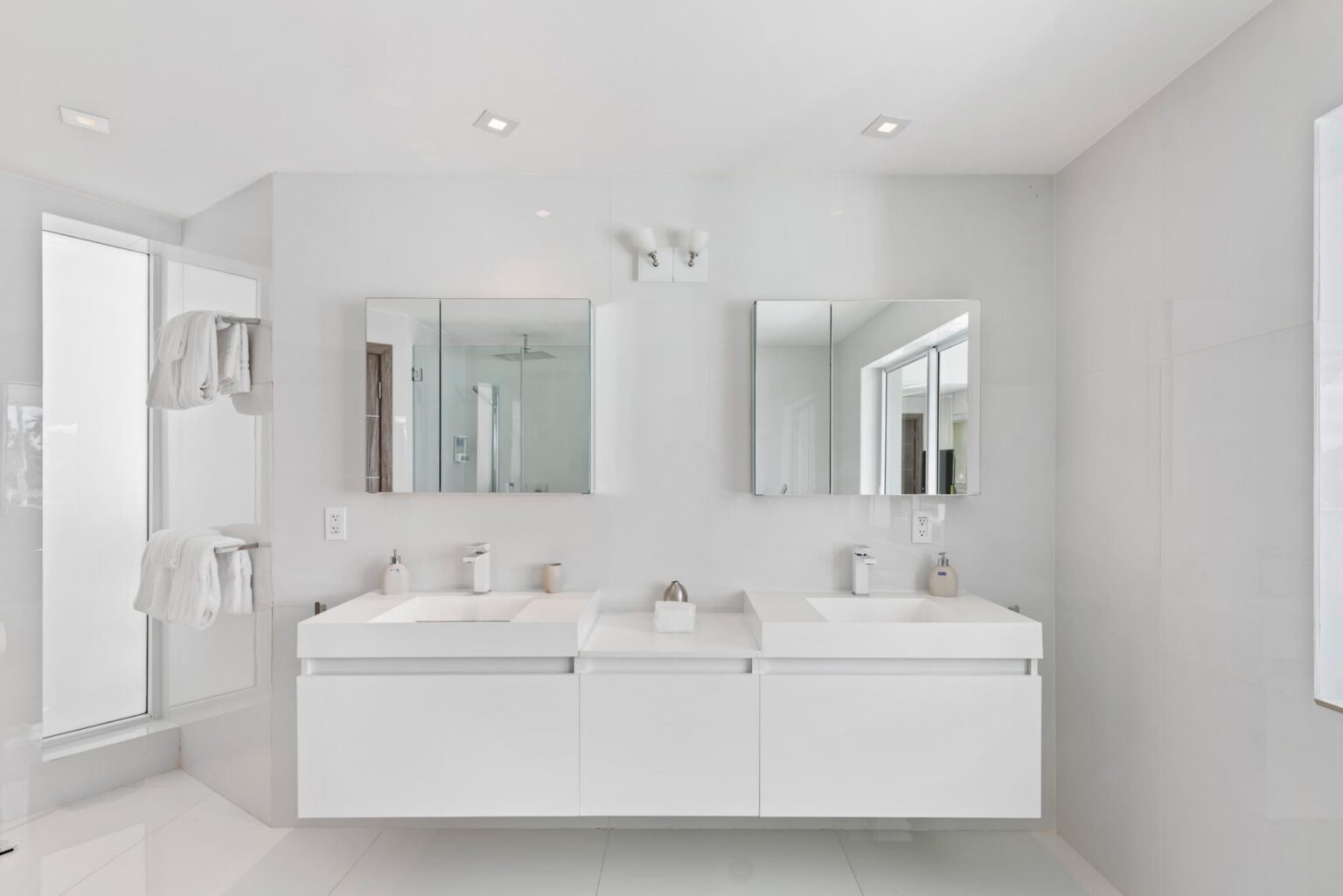 Double-vanity bathroom featuring dual sinks, floating storage cabinetry, oversized wall mirrors, modern lighting, tile flooring, towel storage, and a bright contemporary layout with ample counter space for guest convenience and daily use.