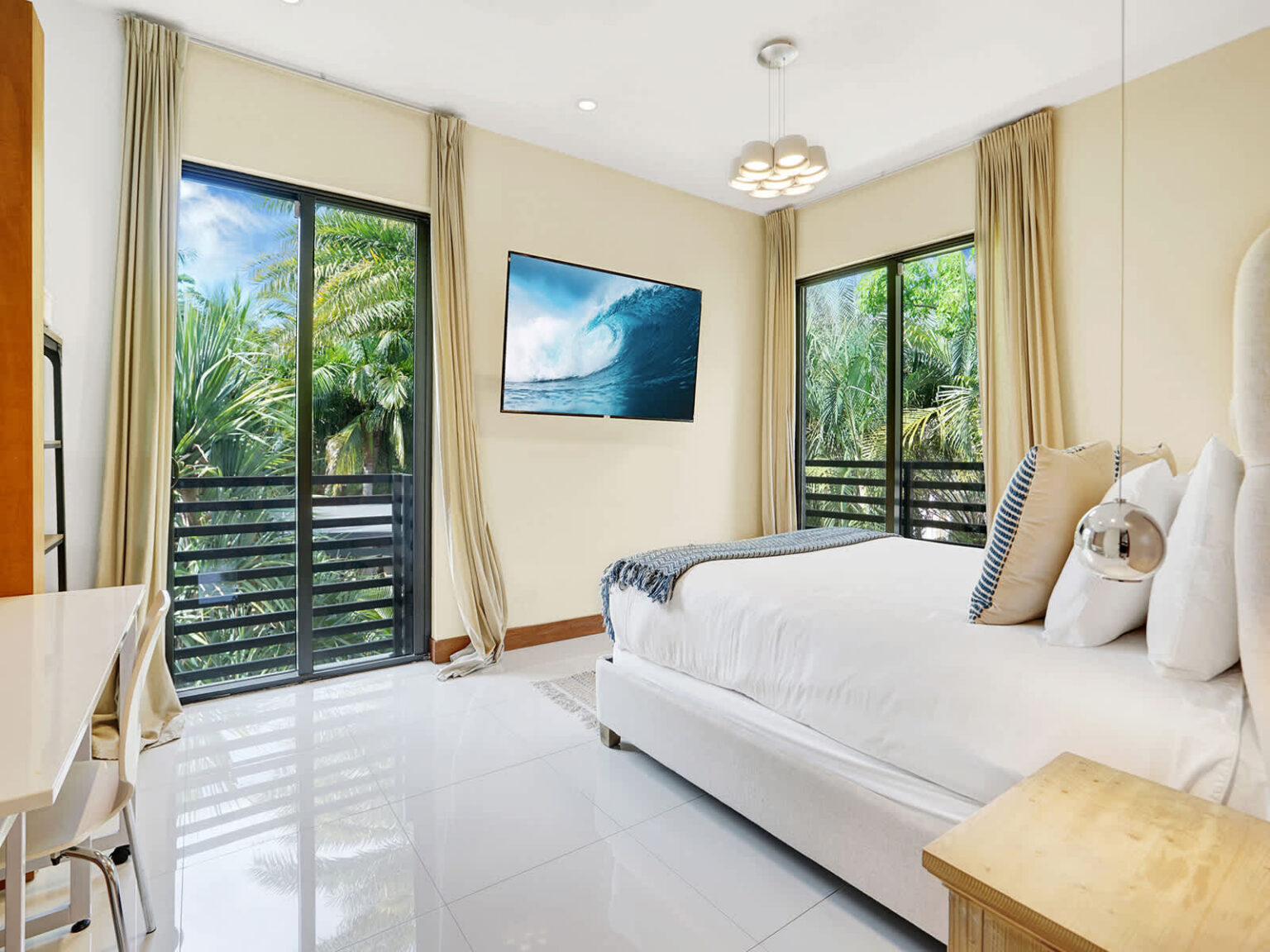 Bright bedroom featuring a king-size bed, floor-to-ceiling windows, and sliding glass doors leading to a covered balcony. Tropical views, abundant natural light, and modern furnishings create a comfortable and relaxing retreat.