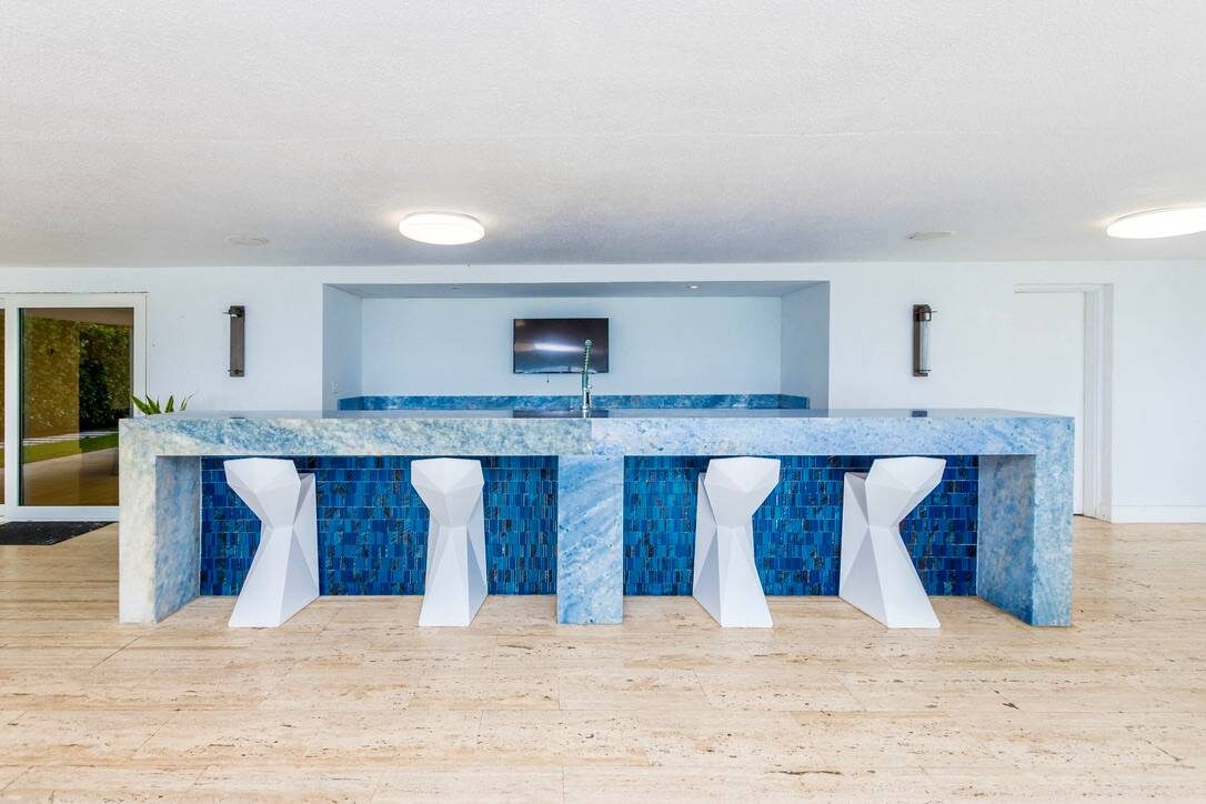 Outdoor entertainment area featuring a custom stone bar with seating for four, mosaic tile accents, wall-mounted TV, recessed lighting, open-concept layout, wood-look tile flooring, and dedicated space for outdoor dining and social gatherings.