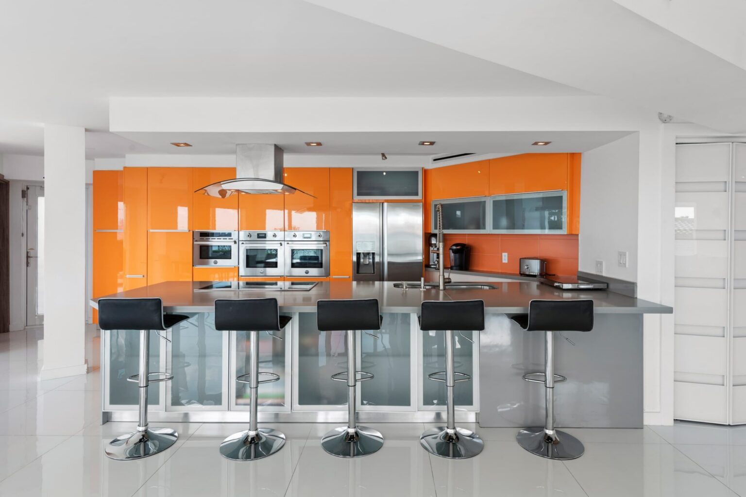 Entertainer’s kitchen featuring a large waterfall-edge island with seating for five, custom high-gloss cabinetry, stainless steel appliances, built-in double ovens, and an open-concept layout designed for dining, cooking, and gathering.