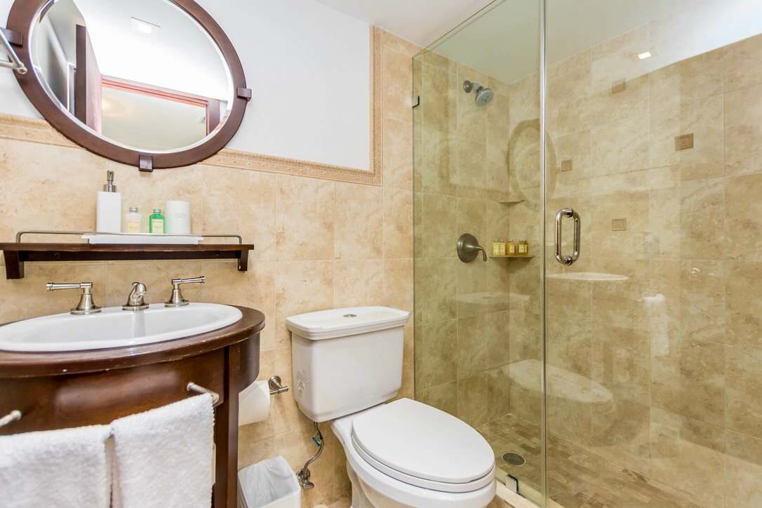 Guest bathroom featuring a glass-enclosed walk-in shower, natural stone tile finishes, pedestal-style vanity with integrated sink, round wall mirror, built-in shower niche, modern fixtures, and a bright, functional layout.