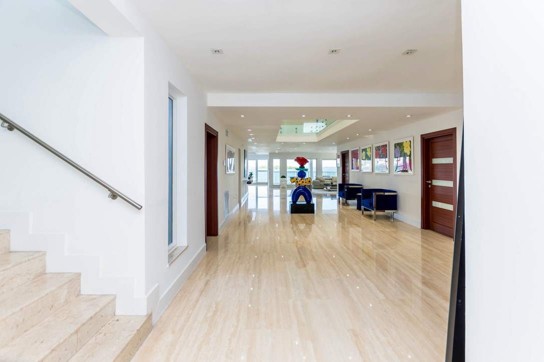 Welcoming entry corridor featuring oversized tile flooring, contemporary artwork, recessed lighting, staircase access, double wood doors, a skylight feature, and an open-concept layout connecting the home's living, dining, and entertainment spaces.