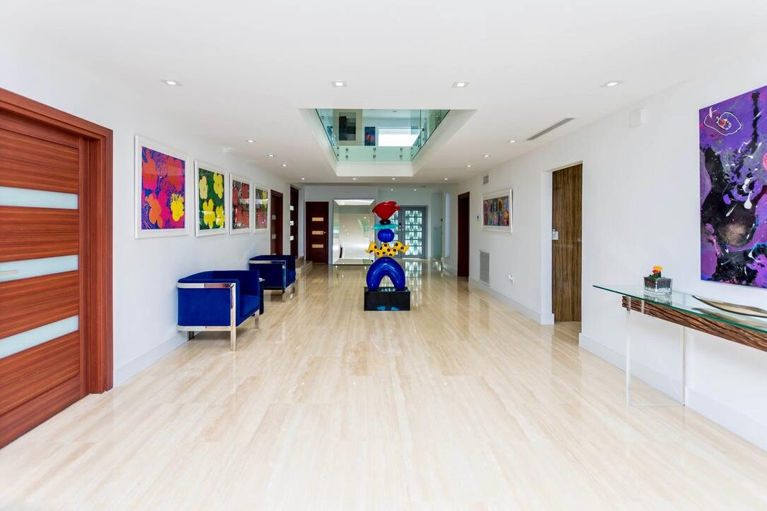 Grand entrance foyer featuring oversized tile flooring, contemporary artwork, accent seating, double interior doorways, recessed lighting, a skylight feature, and an expansive open-concept layout connecting multiple living and entertaining areas.