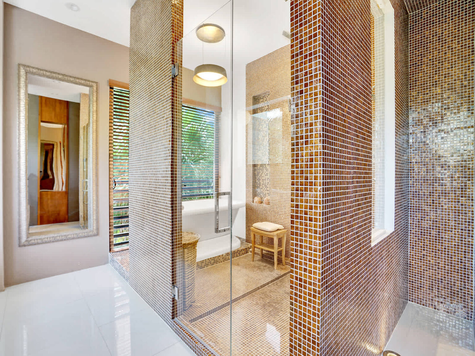 Spa-inspired bathroom entrance featuring a glass-enclosed shower, textured mosaic tile accents, and modern fixtures. Large windows provide natural light, while the open layout and natural materials create a bright, contemporary space.