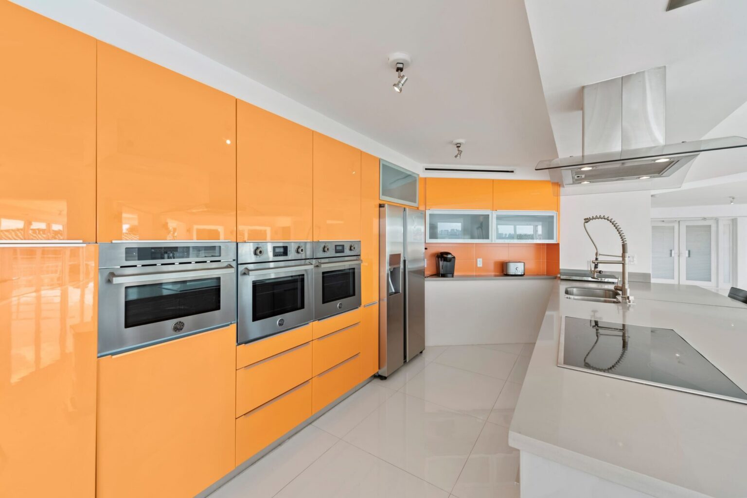 Modern chef’s kitchen featuring custom high-gloss cabinetry, stainless steel appliances, built-in double ovens, expansive quartz countertops, integrated storage, and a functional open layout designed for cooking and entertaining.