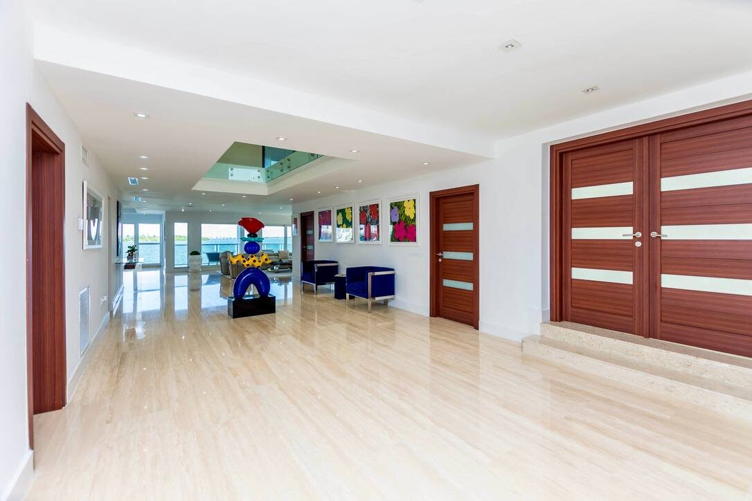 Elegant entry hall featuring oversized tile flooring, contemporary artwork, accent seating, double wood entry doors, recessed lighting, and a spacious open-concept layout that provides access to the home's main living and entertainment areas.