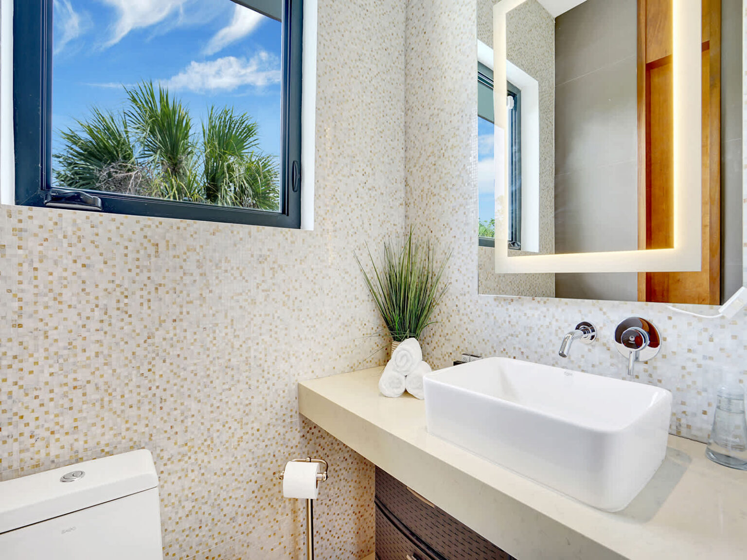 Contemporary bathroom featuring a modern vanity with integrated sink, large framed mirror, and natural stone-textured walls. A frosted window provides natural light and privacy, while clean finishes create a bright, functional space.