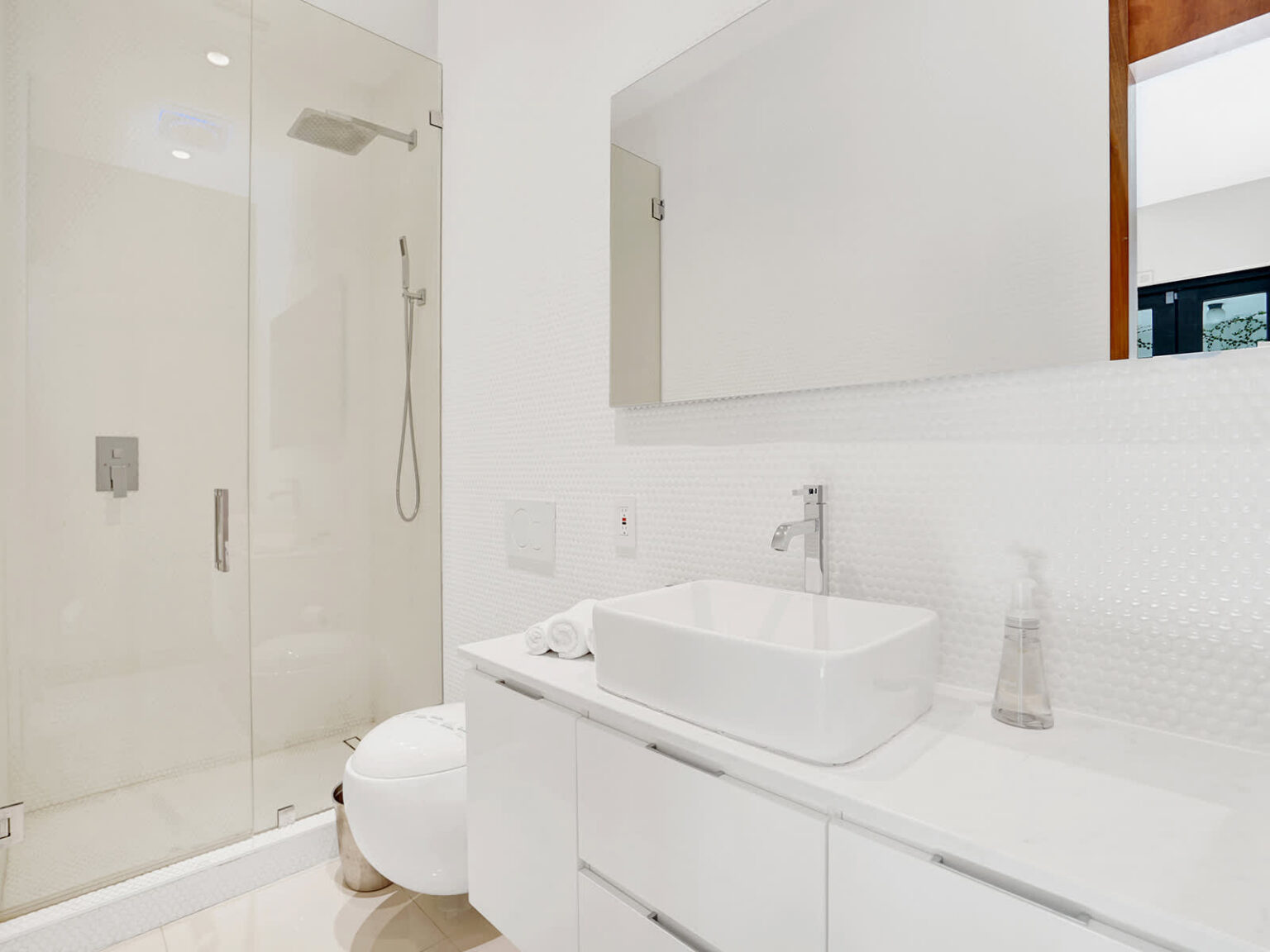 Modern ensuite bathroom featuring a vessel sink vanity, walk-in glass shower, and contemporary fixtures. Clean white finishes, integrated storage, and bright lighting create a functional, streamlined space designed for everyday comfort.
