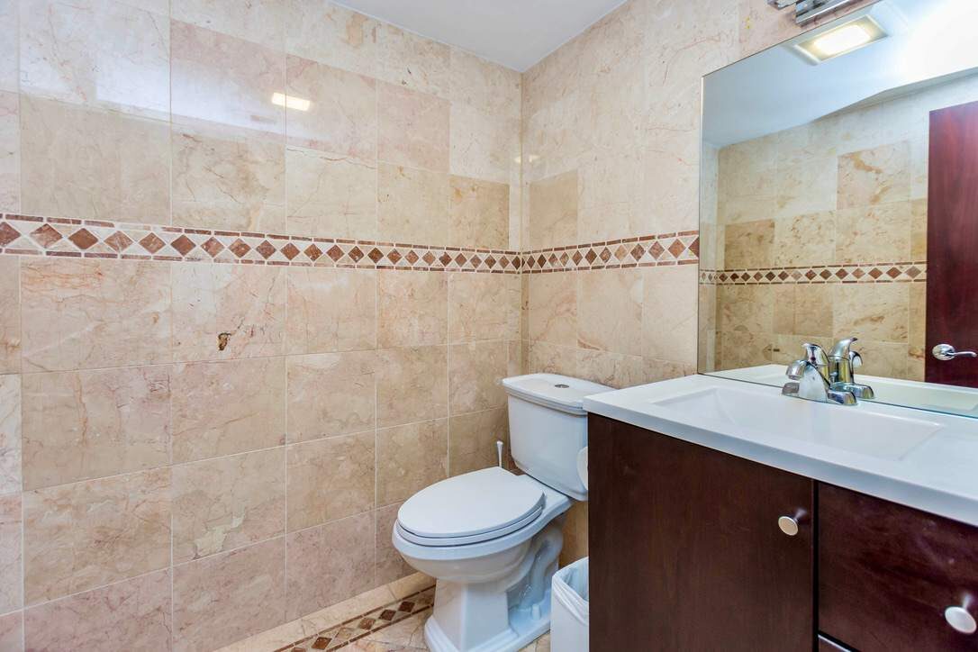 Additional bathroom featuring a single-sink vanity with storage cabinetry, large wall mirror, natural stone tile finishes, modern lighting, tiled flooring, and a clean functional layout with contemporary fixtures and ample counter space.