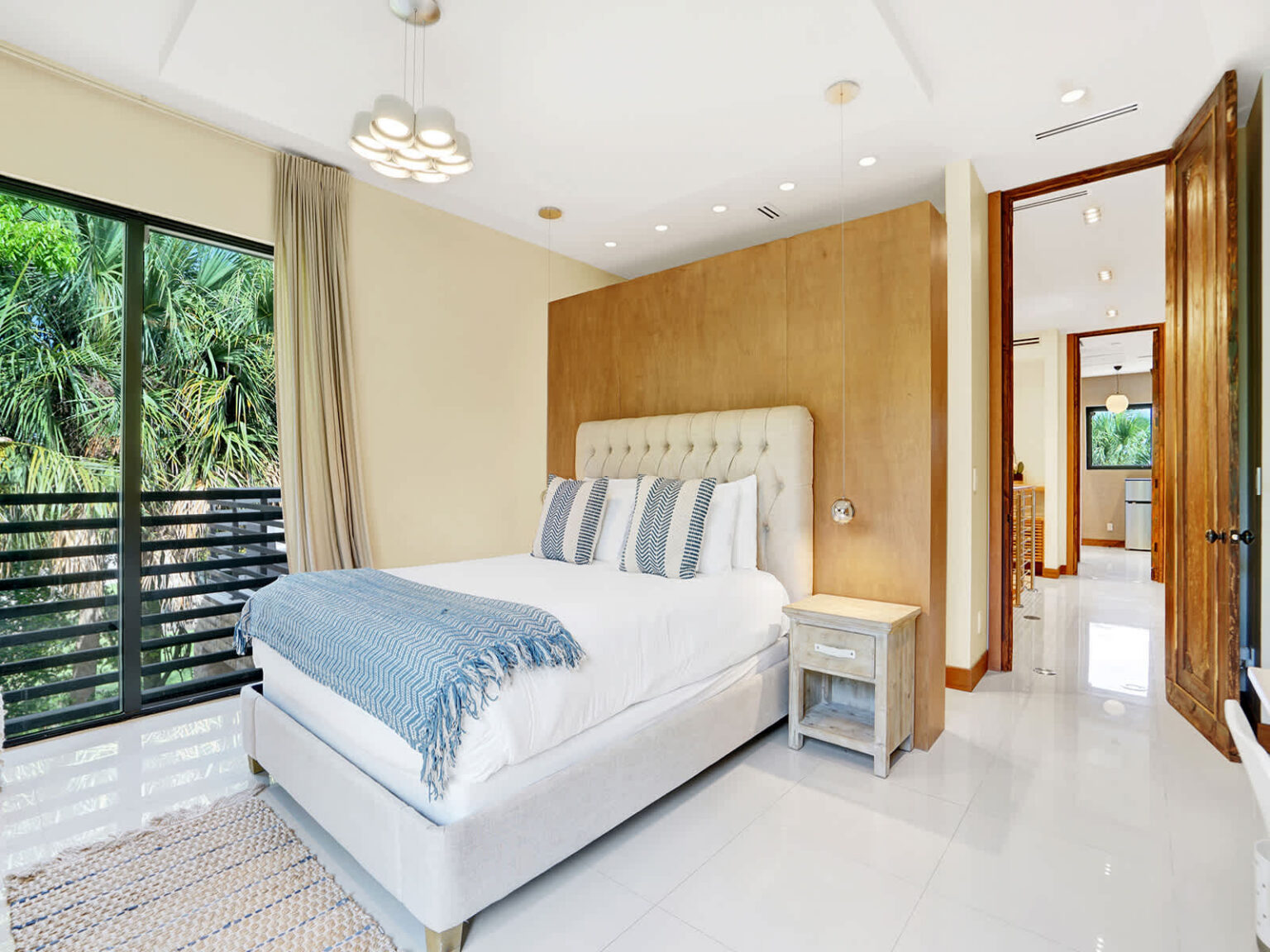 Contemporary bedroom featuring a queen-size bed, wood accent wall, and floor-to-ceiling windows. Natural light, modern furnishings, and a bright open layout create a comfortable retreat, with convenient access to the ensuite bathroom.