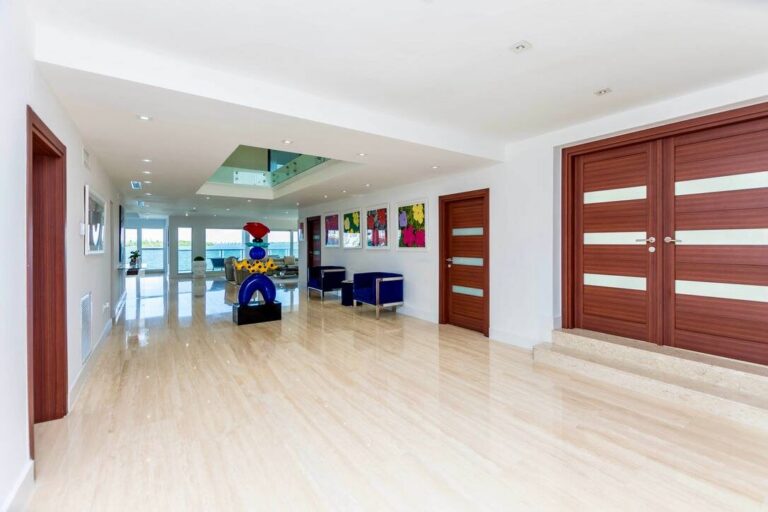 Spacious entrance hall and foyer featuring large-format tile flooring, double front doors, recessed lighting, contemporary artwork, accent seating, interior balcony overlook, and an open-concept layout with natural light throughout.