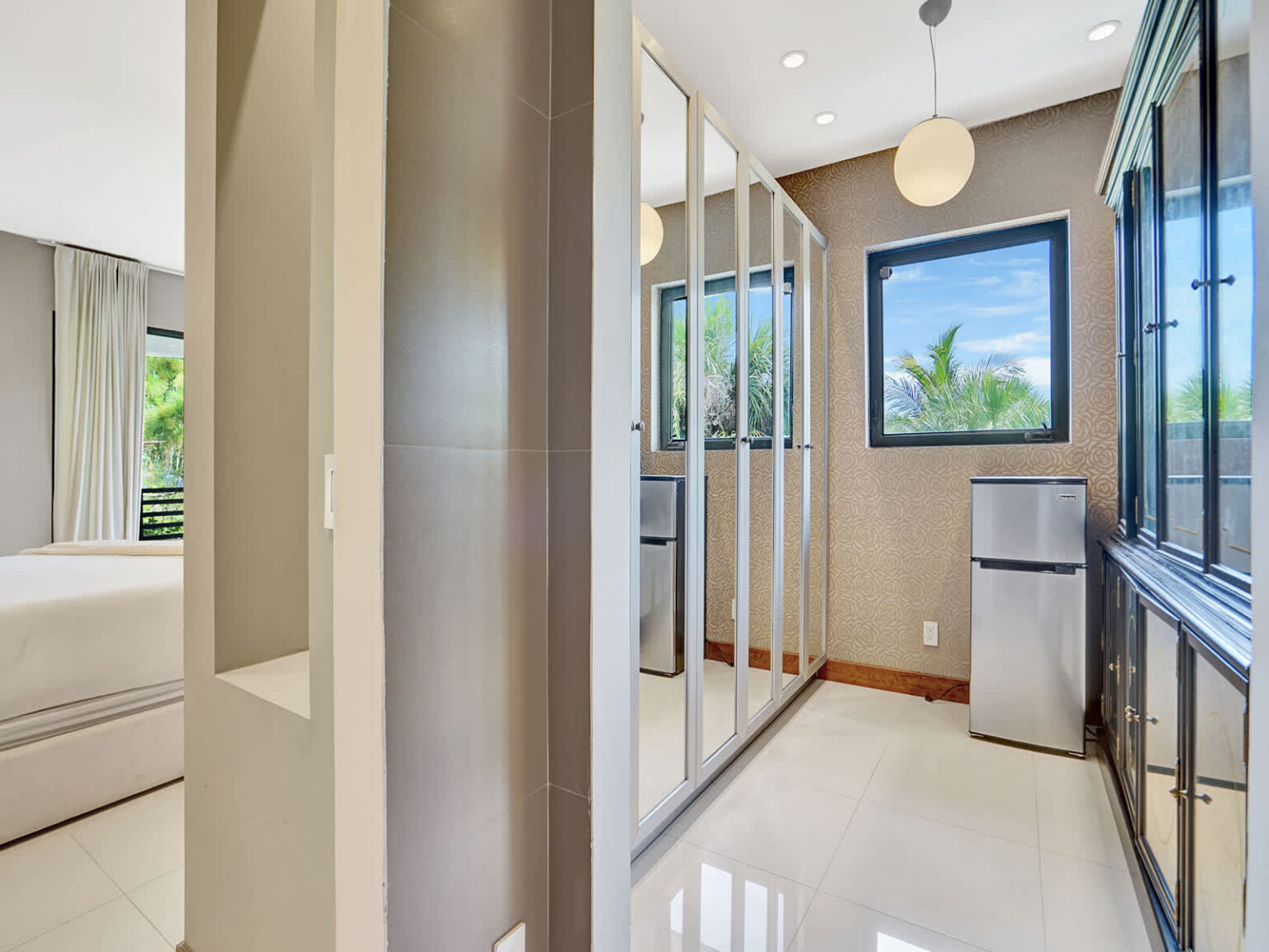 Walk-in closet area featuring mirrored wardrobe doors, custom storage cabinetry, and polished tile flooring. Natural light from the nearby window brightens the space, while the functional layout provides ample storage and organization.