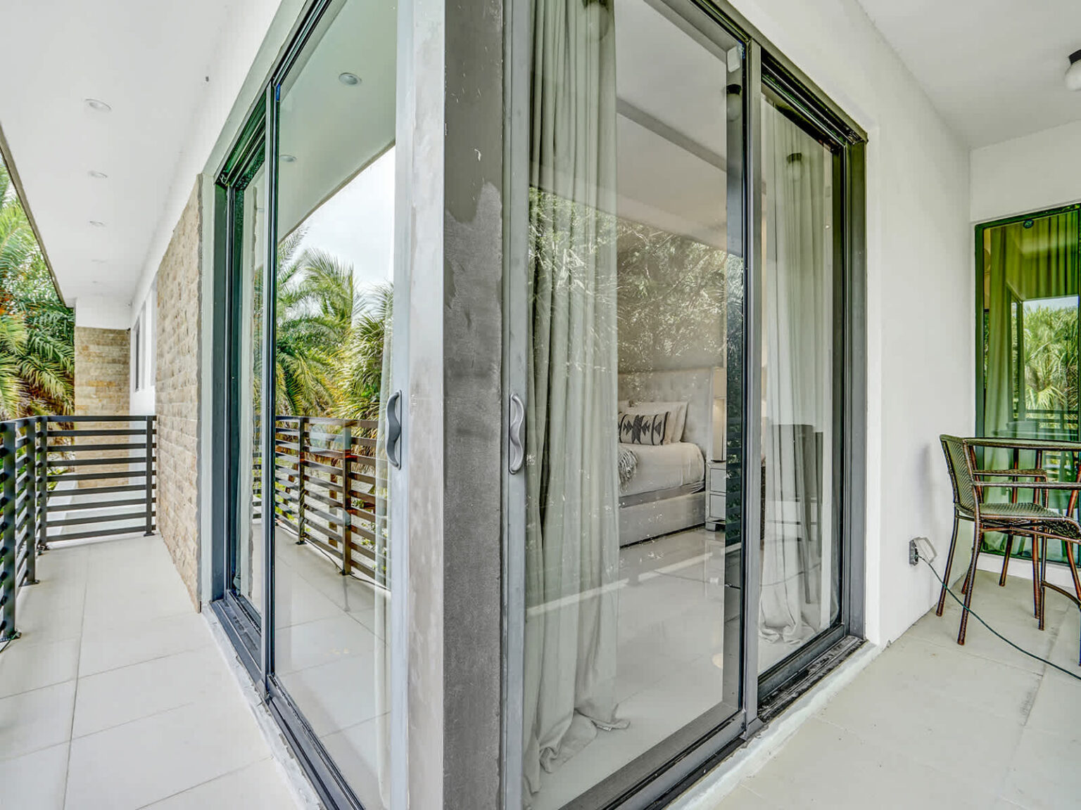Covered second-floor balcony with sliding glass doors, modern architecture, and views of tropical landscaping. This outdoor extension of the bedroom provides natural light, fresh air, and a seamless connection between indoor and outdoor spaces.