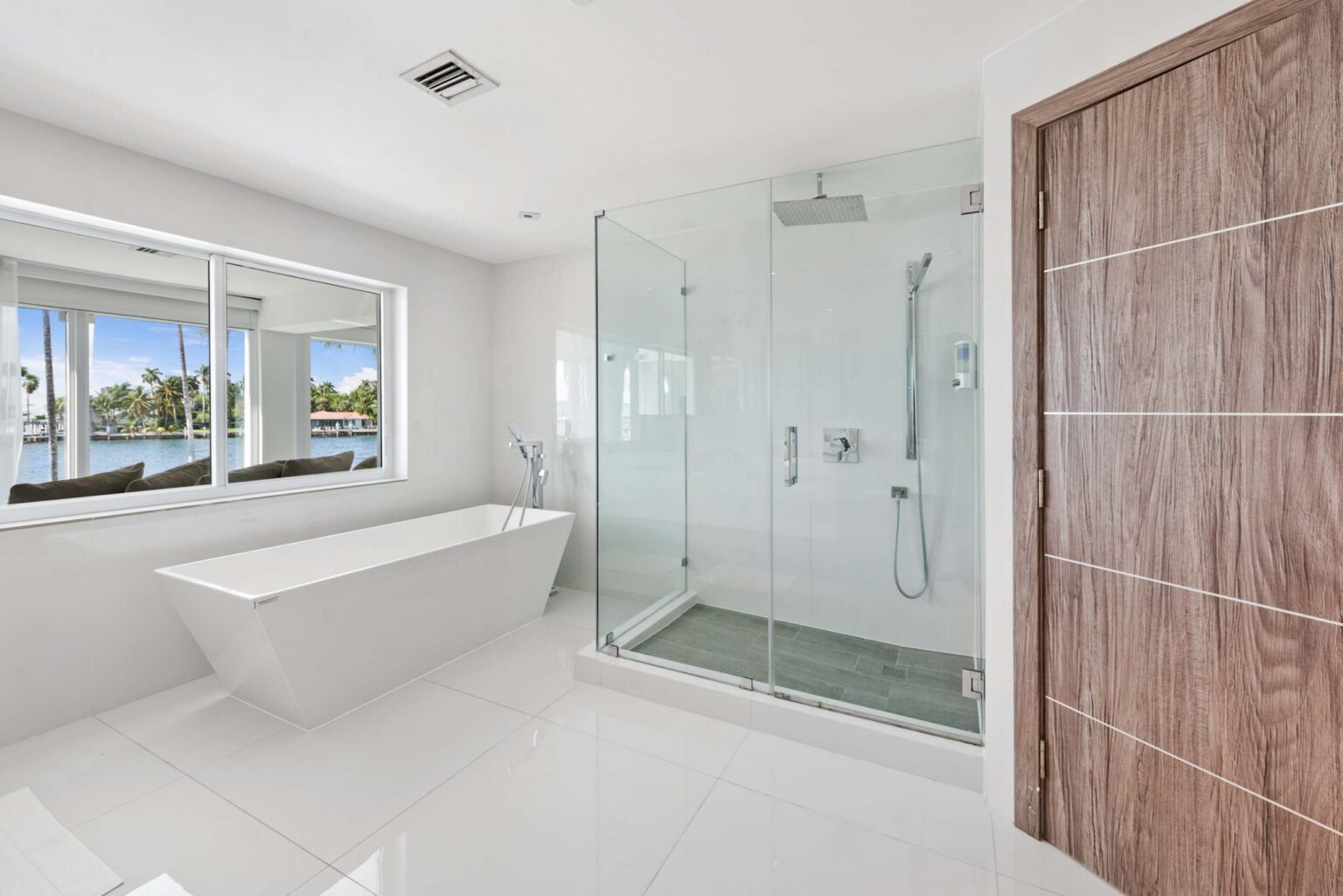 Spa-inspired primary bathroom featuring a freestanding soaking tub, glass-enclosed walk-in shower, large picture window, tile flooring, modern fixtures, and a bright open layout with dedicated bathing and wellness space.