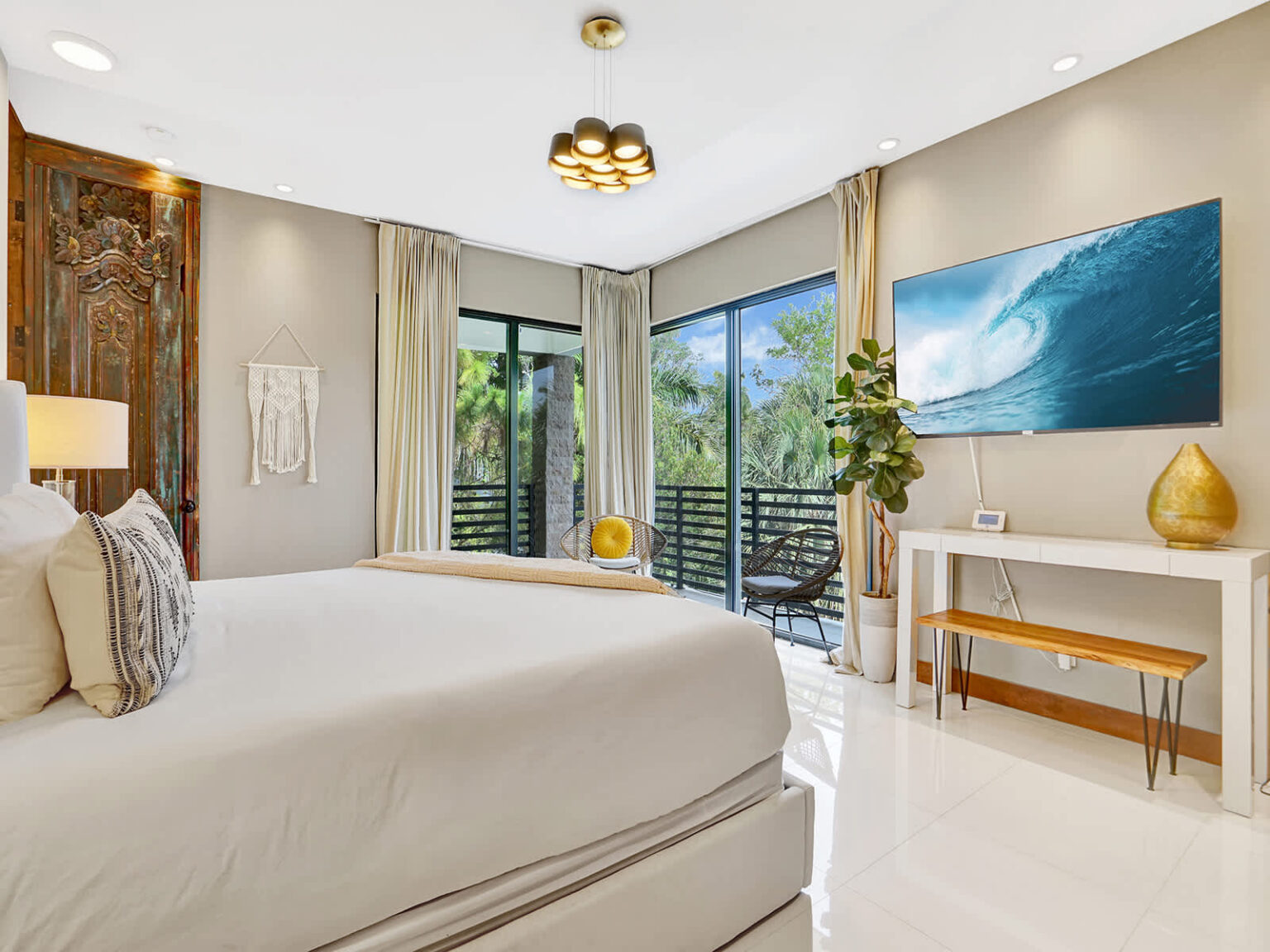 Bright bedroom featuring a king-size bed, floor-to-ceiling windows, and sliding glass doors with tropical views. Modern furnishings, natural light, and a spacious layout create a comfortable retreat with seamless indoor-outdoor connection.