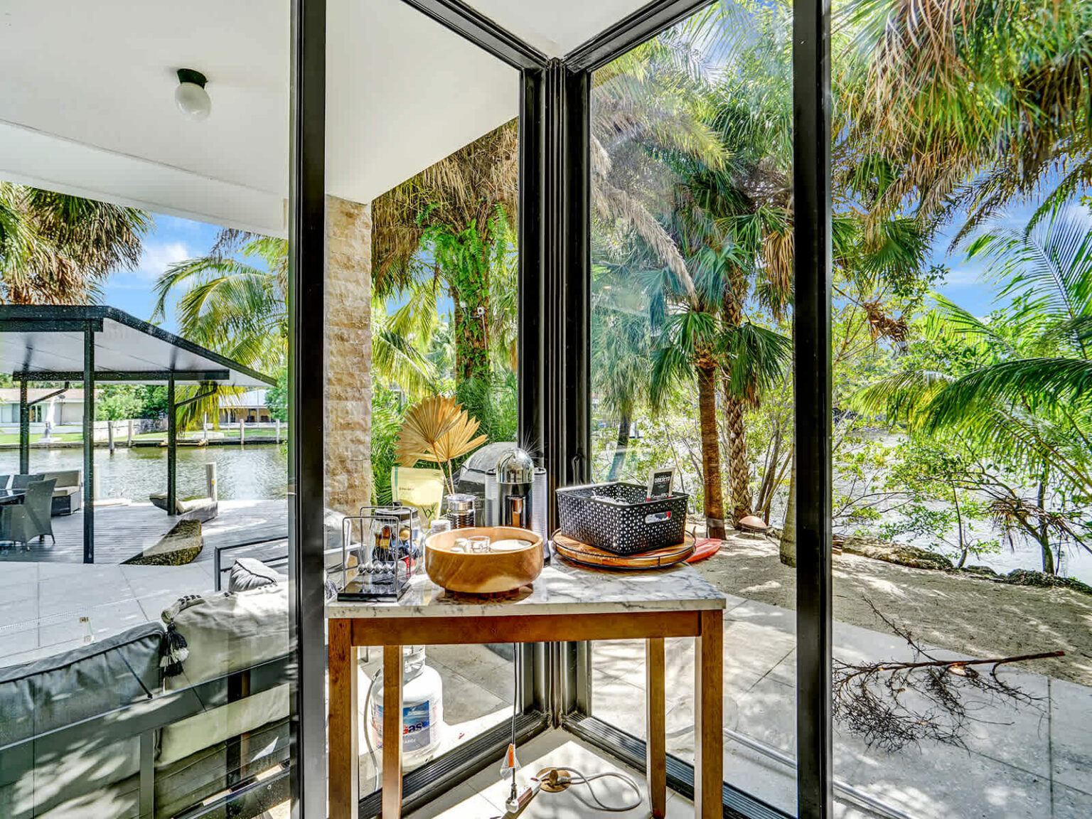 Breakfast nook with a wood dining table positioned beside floor-to-ceiling windows overlooking tropical landscaping. Filled with natural light, this intimate seating area offers garden views and convenient access to the outdoor patio.